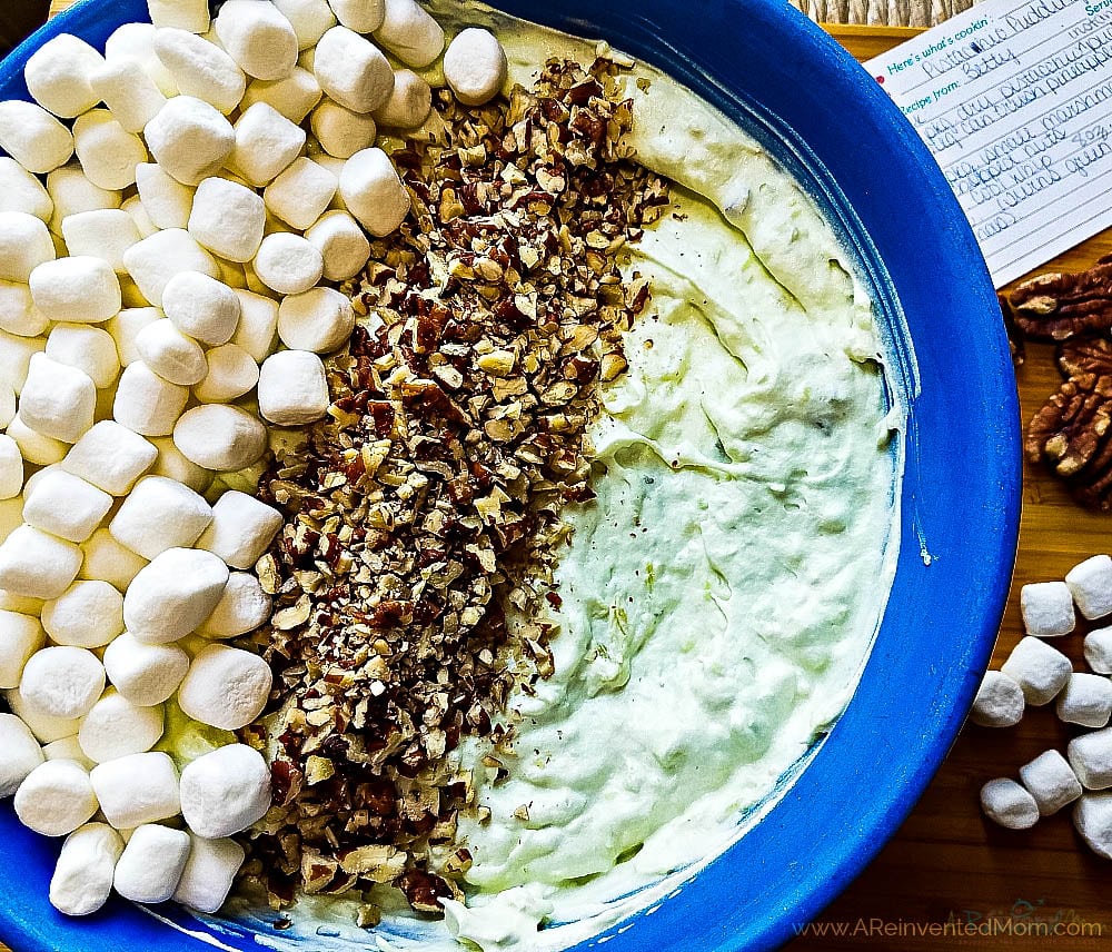 Adding marshmallows and chopped nuts to the pistachio fluff salad mixture.