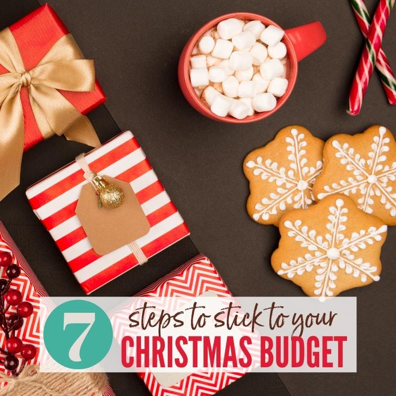 Wrapped presents, iced snowflake cookies, red mug filled with hot cocoa & marshmallows. and candy canes on a brown background. 7 Steps to Stick to Your Christmas Budget | A Reinvented Mom