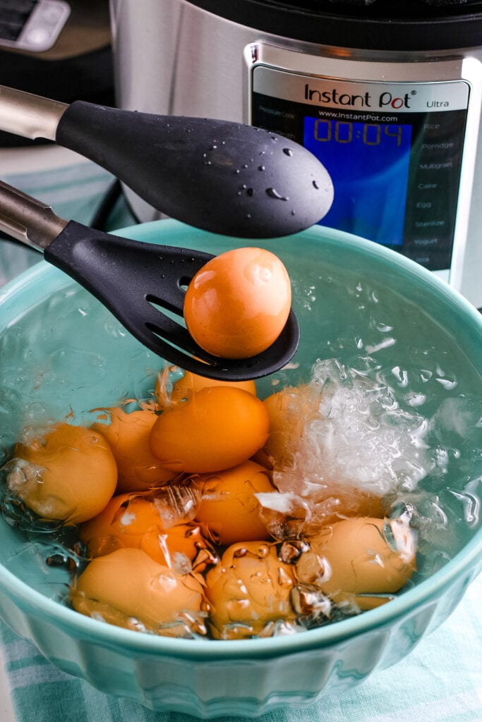Tongs removing an egg from a blue bowl filled with ice & hard boiled eggs | Instant Pot Hard Boiled Eggs | A Reinvented Mom
