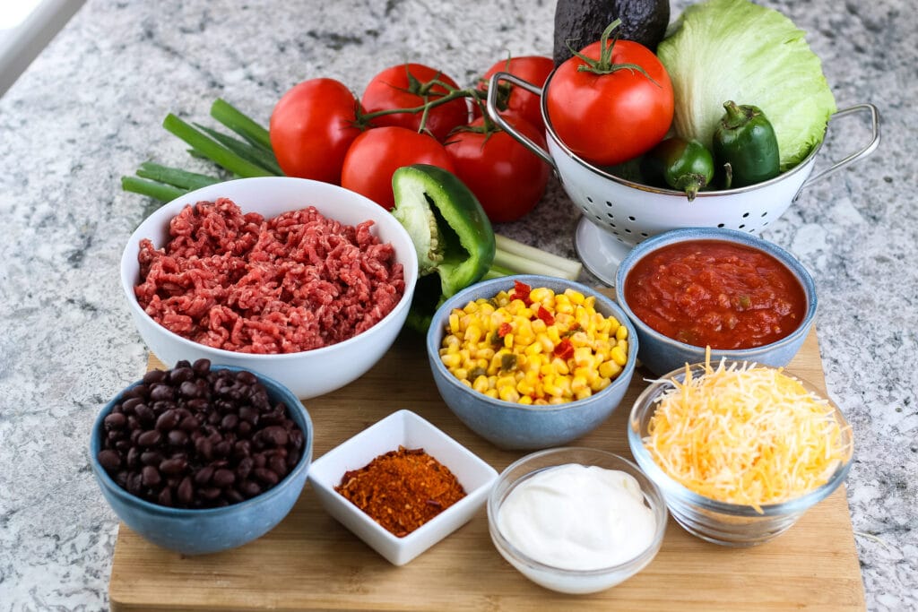 Bowls filled with ingredients for Homemade Taco Salad on wooden surface | A Reinvented Mom