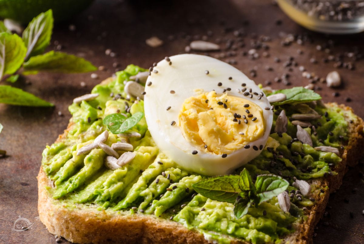 A slice of bread with mashed avocado, hard boiled egg slice & sunflower seeds on a stone background. Recipes with Boiled Eggs | A Reinvented Mom