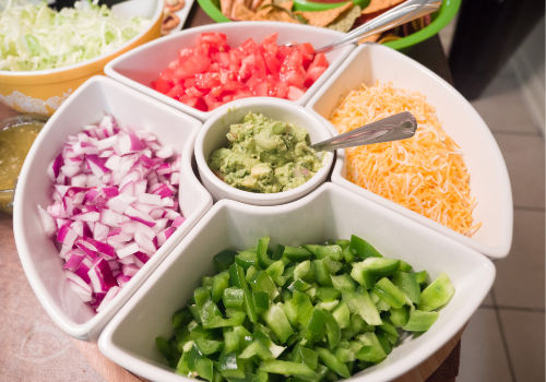 Chopped onions, peppers, tomatoes, shredded cheese & guacamole in a divided bowl. | How to Throw a Taco Party | A Reinvented Mom