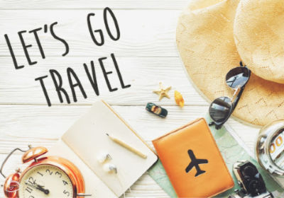 Various travel items on a white wooden flatlay with Let's Go Travel.