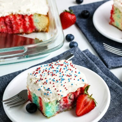 Slices of 4th of July Poke Cake on white plates & blue napkins with full cake in the background | A Reinvented Mom