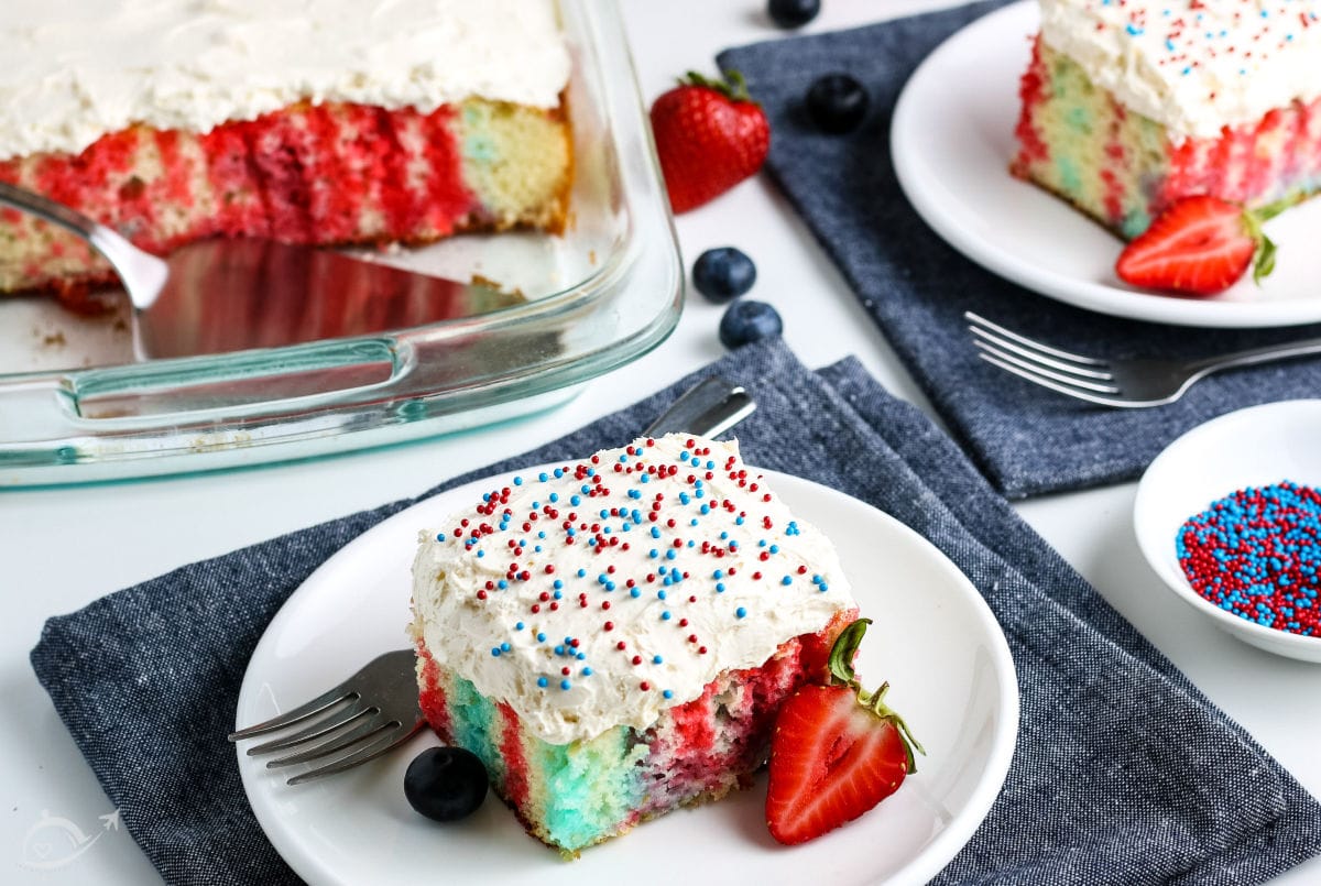 Slices of 4th of July Poke Cake on white plates & blue napkins with full cake in the background | A Reinvented Mom