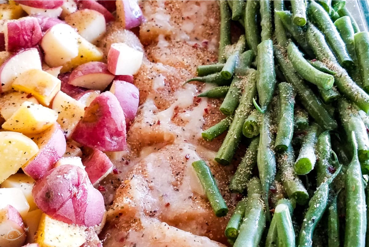 chicken potato green bean bake in a glass dish topped with italian dressing seasoning drizzled with butter