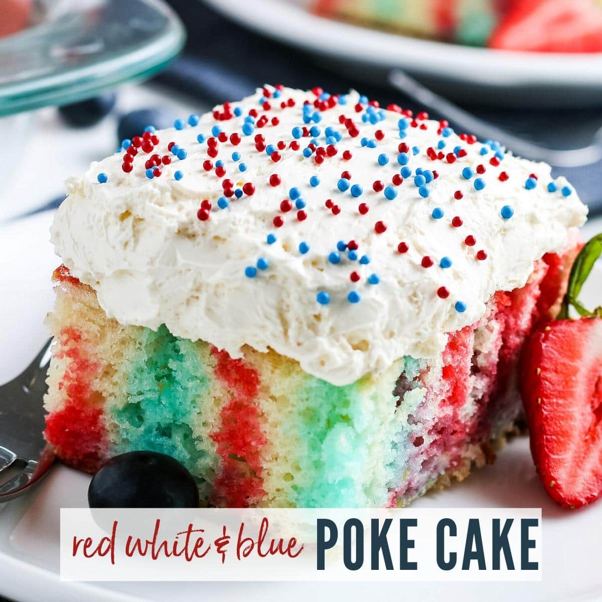 Closeup view of a slice of red, white & blue poke cake with strawberry & blueberry | A Reinvented Mom