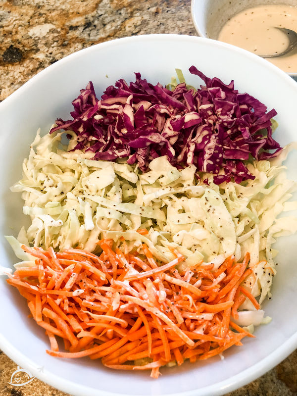 shredded carrots, red cabbage, and regular cabbage in a white bowl ready to make southern coleslaw