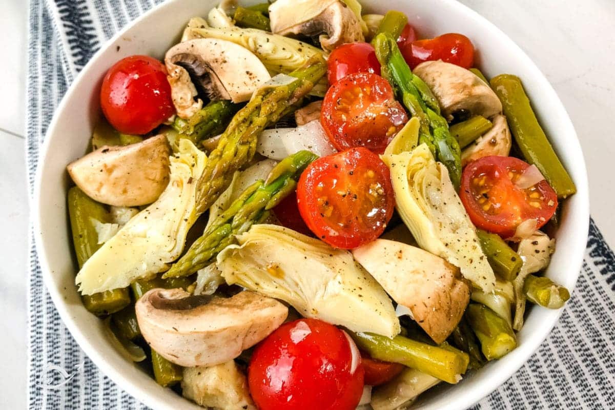 Easy vegetable salad in a white bowl sitting on top of a blue striped dish towel. 