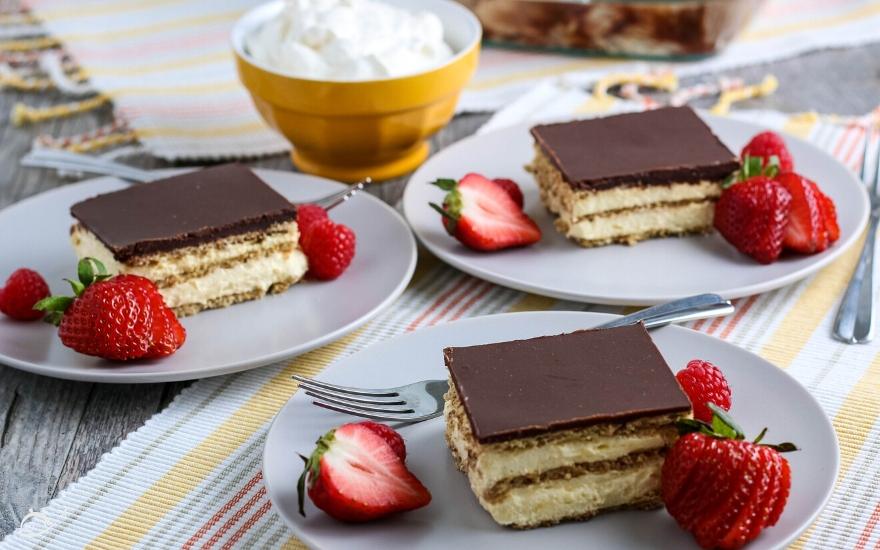 Three white plates with slices of no bake chocolate eclair cake next to strawberries as a garnish. 