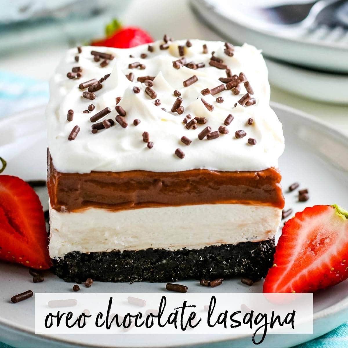 Slice of Oreo Chocolate Lasagna with sliced strawberries on a white plate with graphic overlay. 