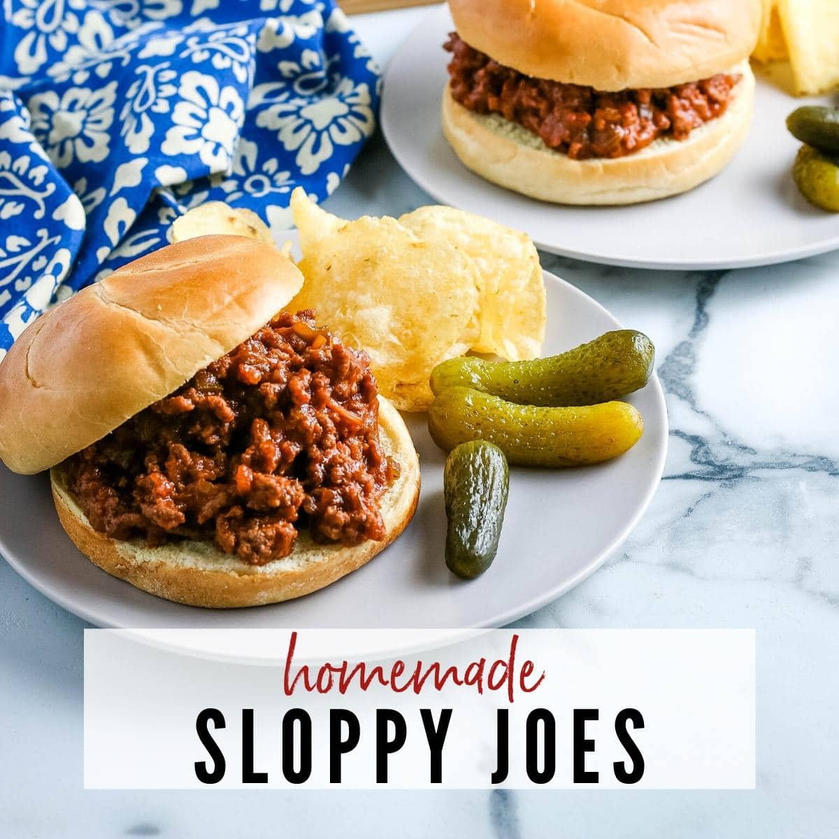 Sloppy Joes with chips and pickles on a white plate with blue flower napkin