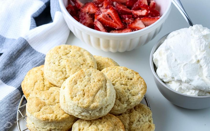 Buttermilk biscuits next to a bowl of strawberries and whipped cream