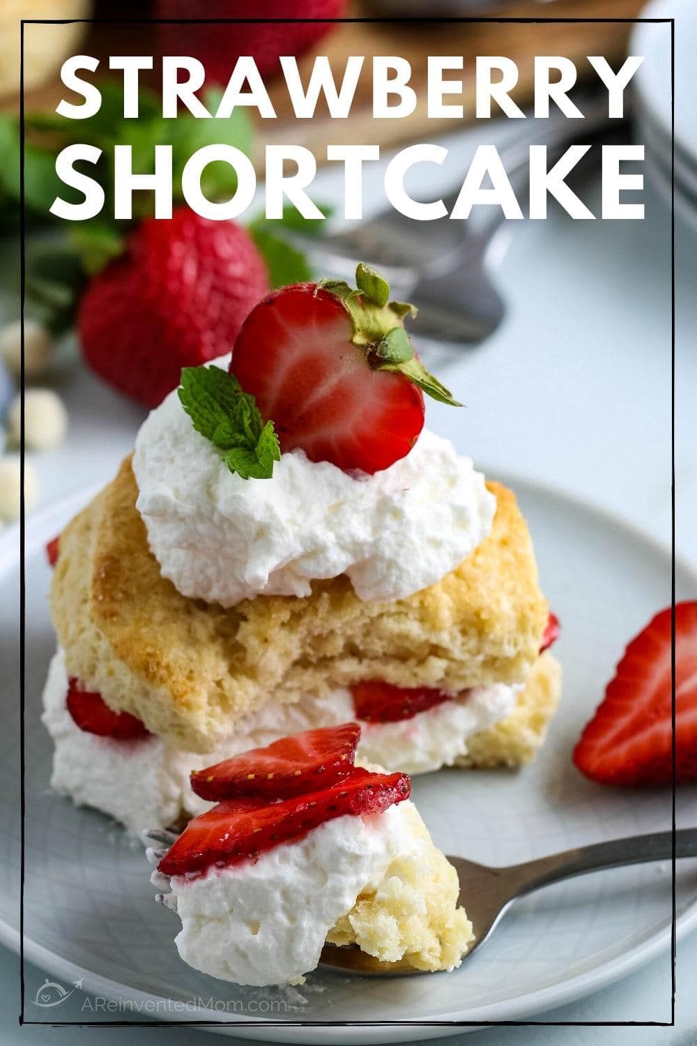 A bite of Strawberry Shortcake on a fork with sliced biscuit, whipped cream and strawberries on a white plate.