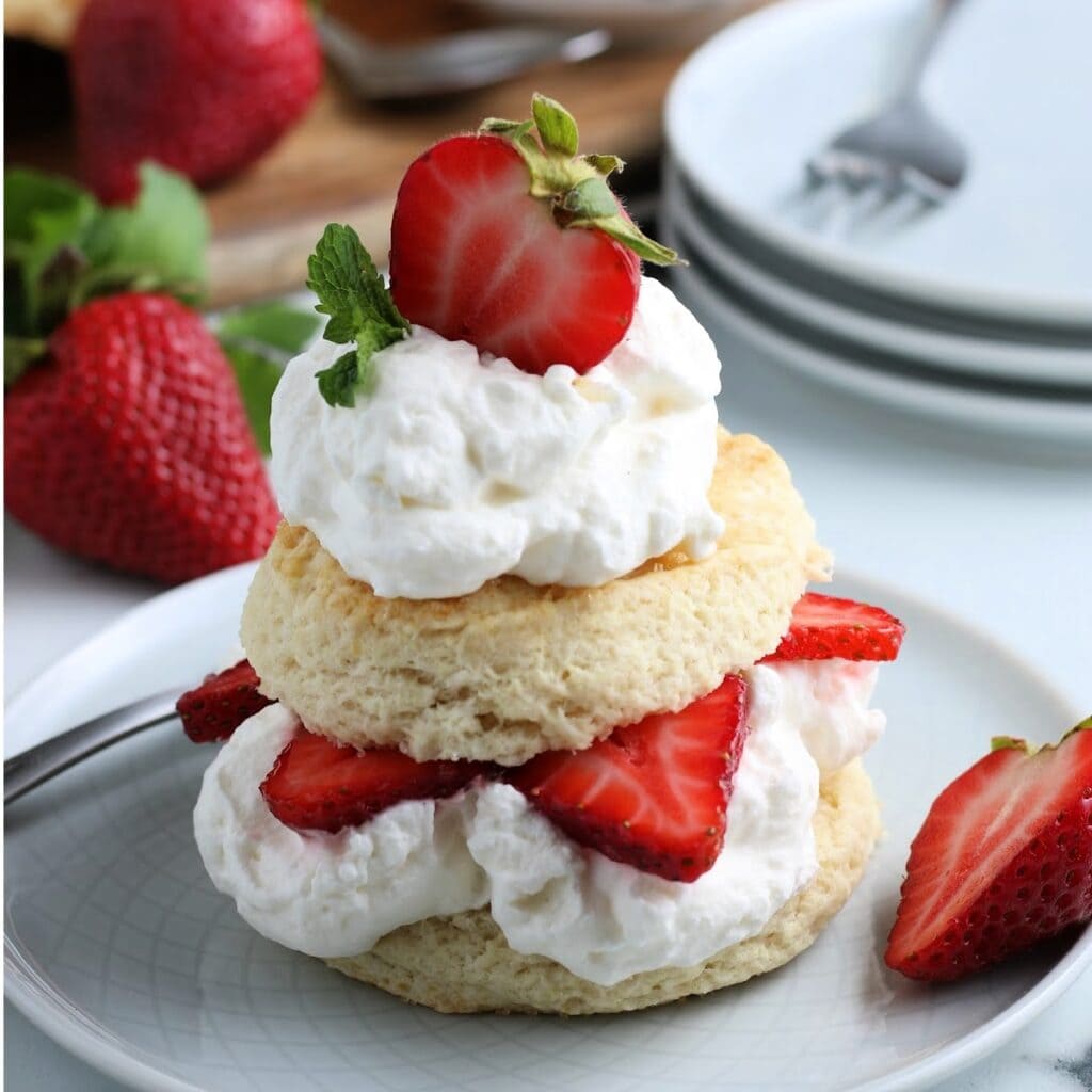 A closeup of biscuit strawberry shortcake, a layered dessert topped with fluffy cream and half a fresh strawberry.