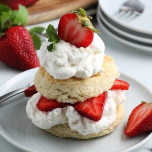 Strawberry shortcake made with biscuit, strawberry and whipped cream layers, on a white plate.
