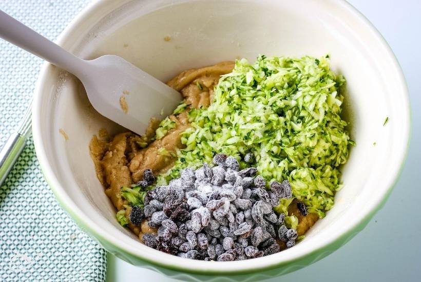 ingredients for zucchini muffins in a green and white bowl with a rubber spatula