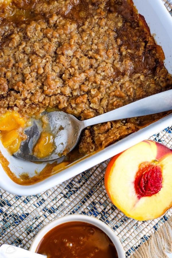 top view of peach crumble with an oat topping in a white casserole dish with a spoon