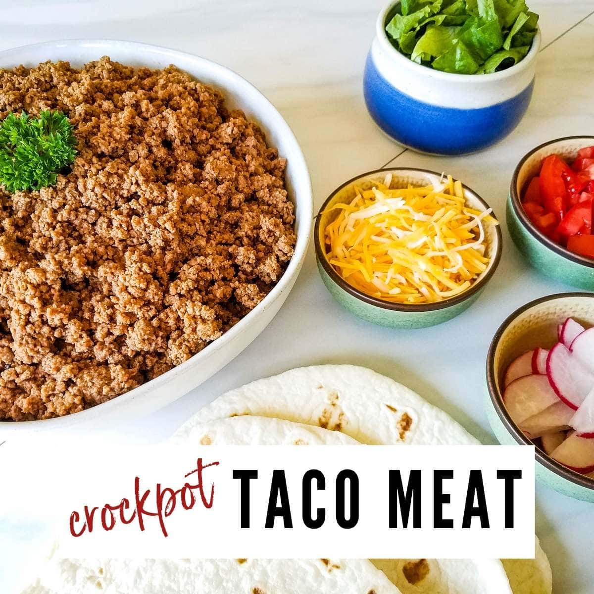 Cooked meat in a white bowl, small bowls of cheese, radishes, lettuce& tomatoes and tortillas on a white counter top with Crockpot Taco Meat graphic overlay.