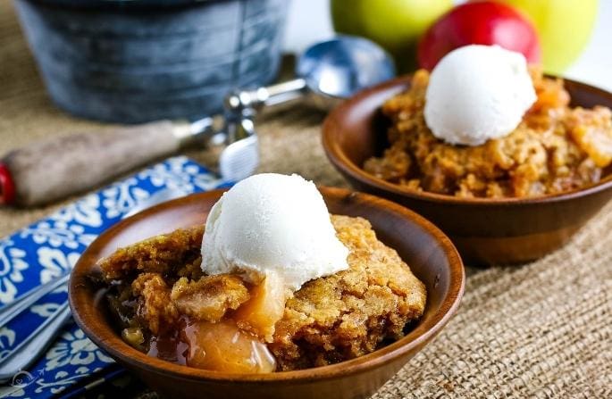 2 wooden bowls filled with apple dump cake and a scoop of vanilla ice cream