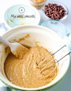 Graham cracker layer mixed in a white bowl with mixing beaters leaned against the side.