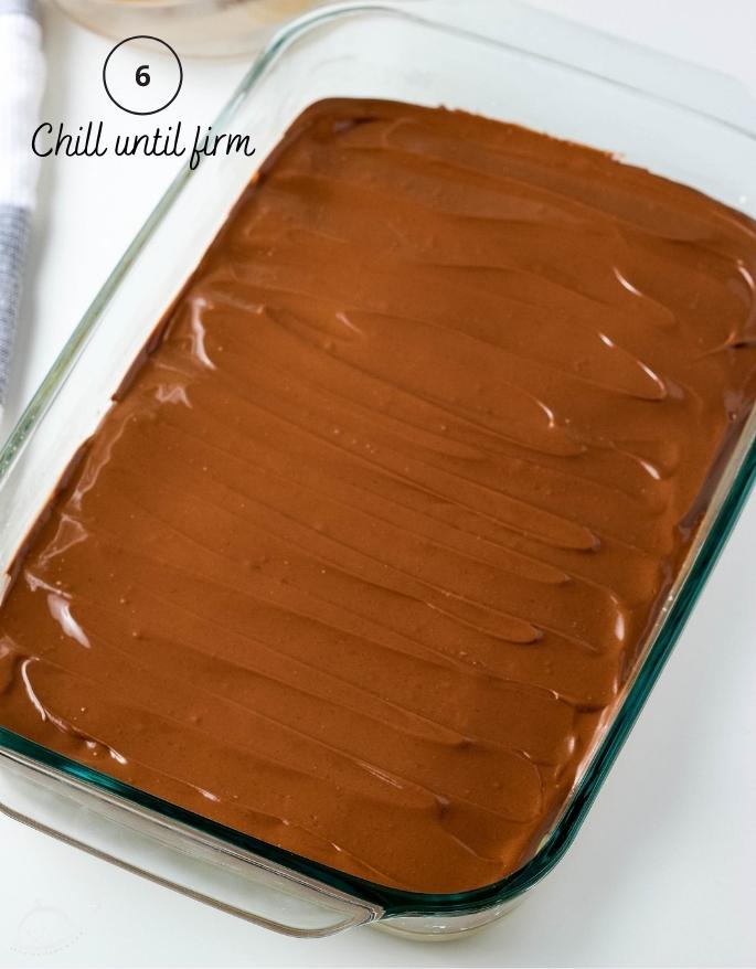 Peanut butter squares with chocolate frosting ready to chill in a baking dish.