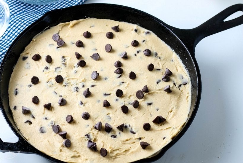 Chocolate chip cookie dough in a cast iron pan before baking.