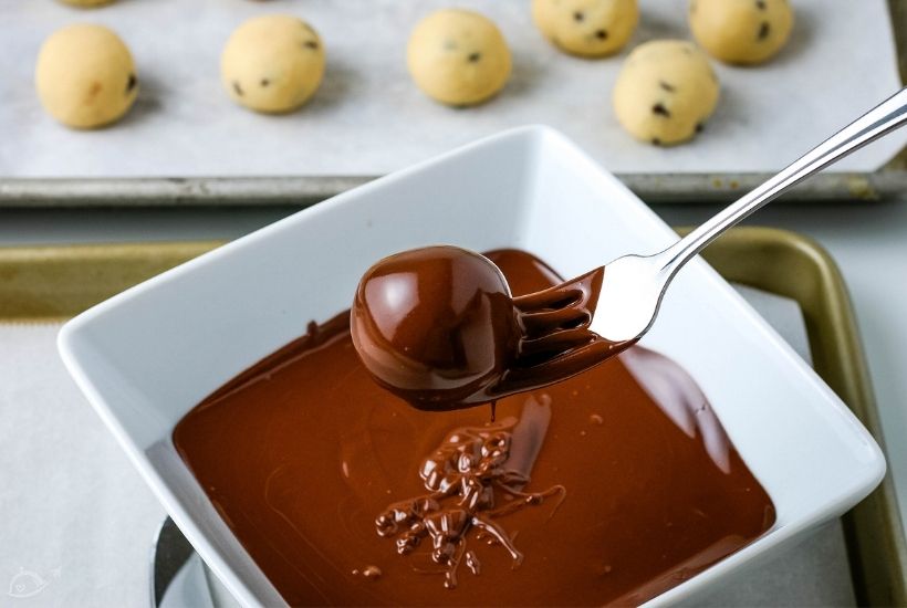 cookie dough bite being dipped in melted chocolate on a fork