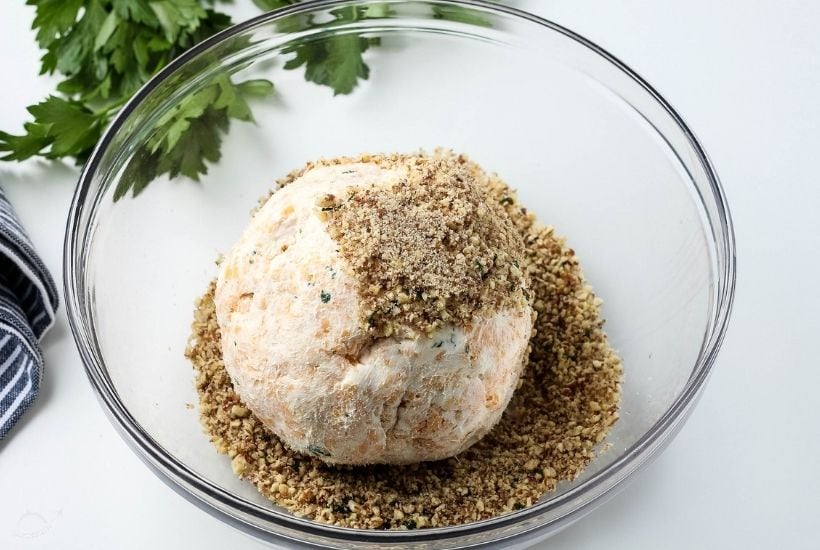 cheese ball sitting in a glass bowl being covered in pecans