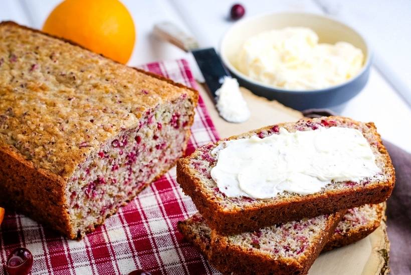 cranberry orange loaf next to three slices that have been cut with the top one with butter.