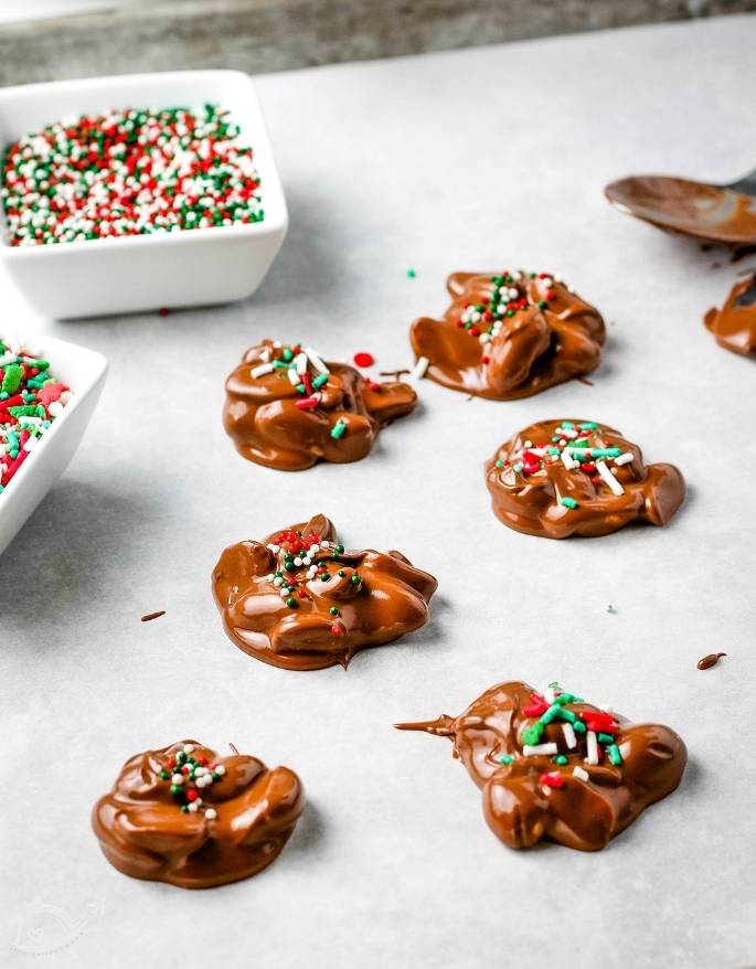 Christmas crack candy cooling on parchment paper next to two bowls of sprinkles
