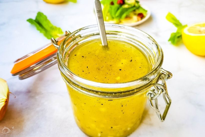 close up of homemade poppyseed vinaigrette in a glass jar next to a lemon