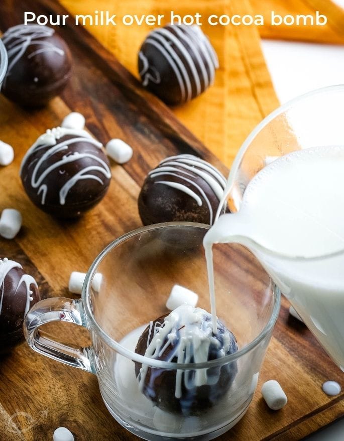 pouring milk over a hot chocolate bomb in a glass mug