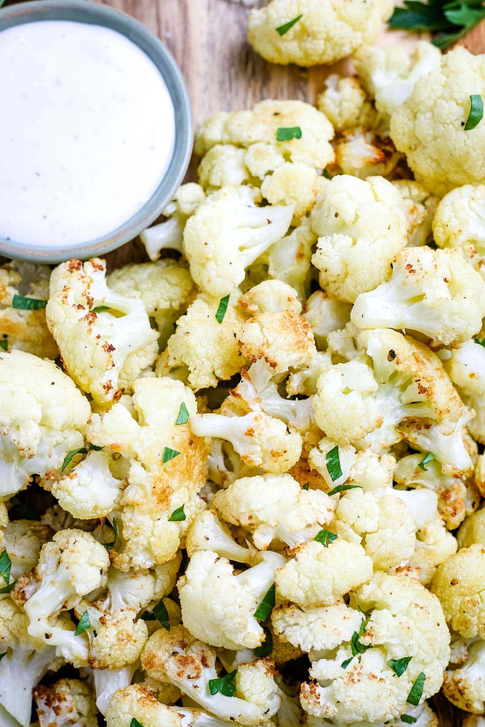 close up of cooked air fryer cauliflower on a wood cutting board with green garnish