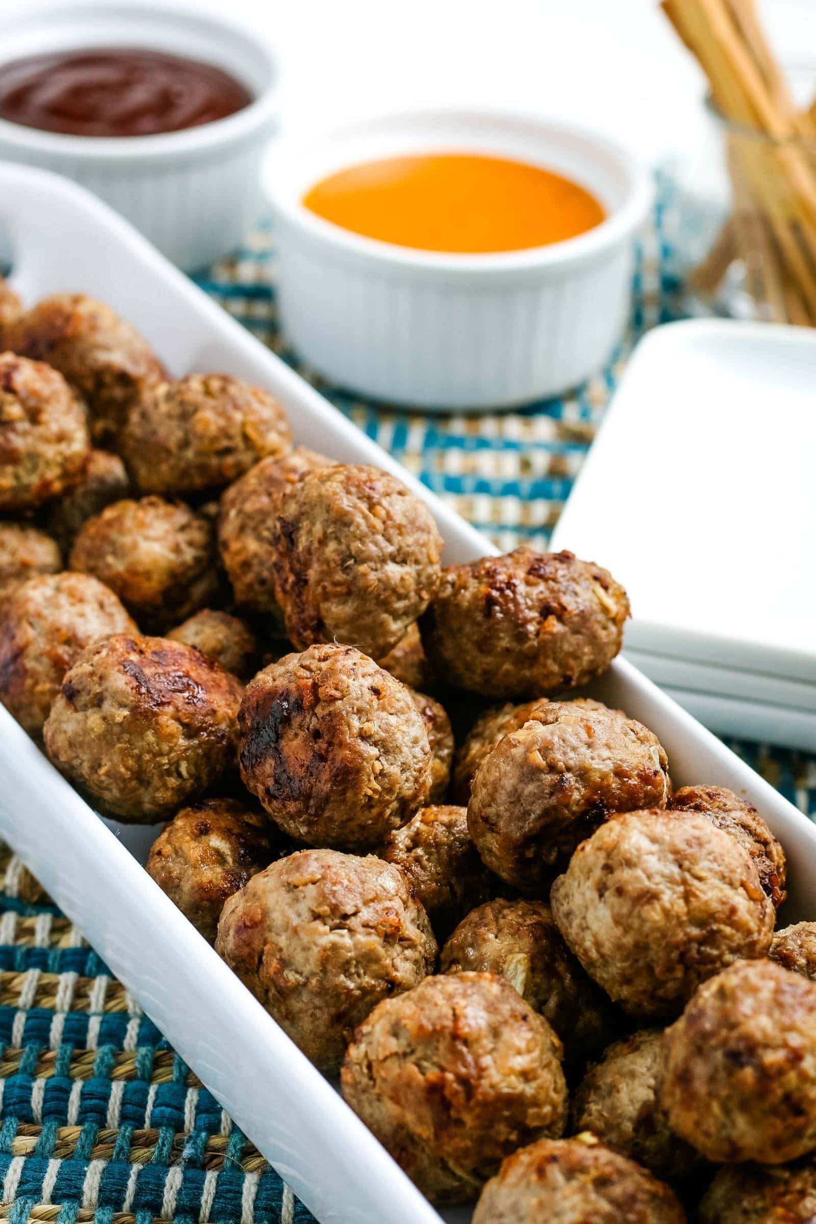 cooked air fryer meatballs on a white plate with dipping sauces in the background