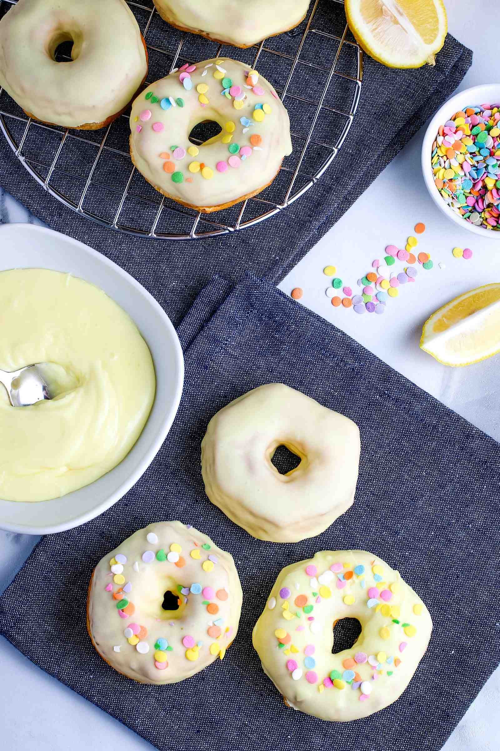 frosted donuts with sprinkles on a black napkin with bowls of frosting and sprinkles