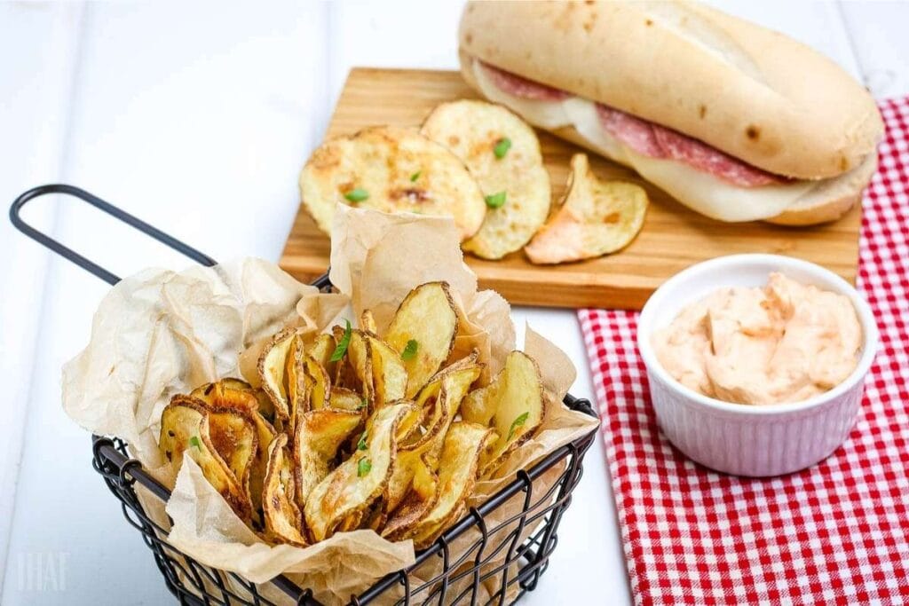 Close up view of air fryer potato chips in a basket and on a board next to a sandwich.