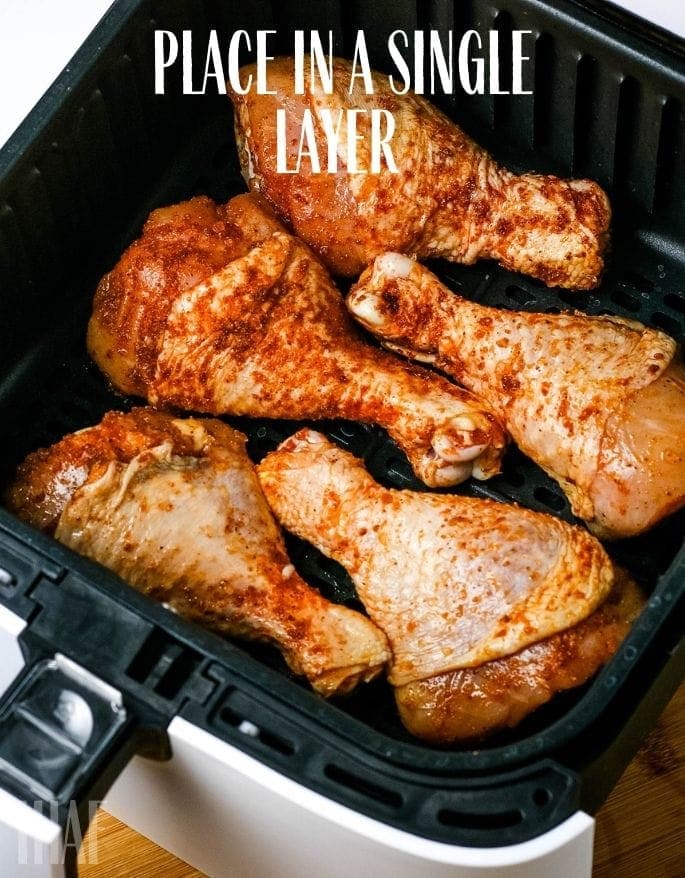 seasoned chicken legs placed in air fryer with text overlay