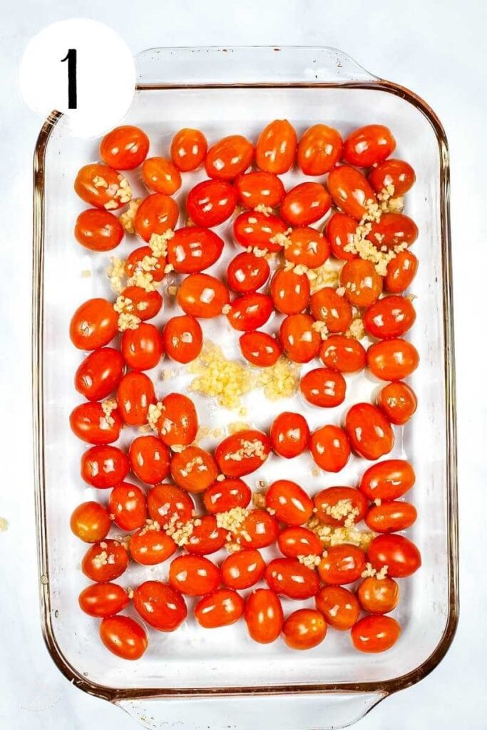 Top view of cherry tomatoes and minced garlic in a glass baking dish.