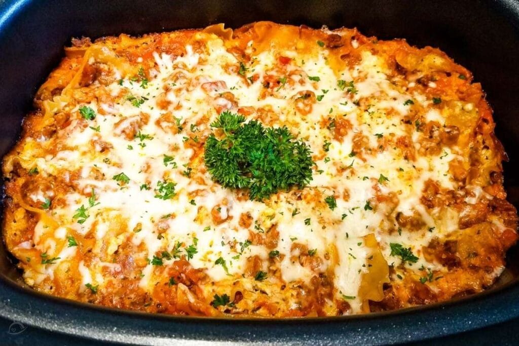 uncut cooked lasagna in crockpot with parsley garnish