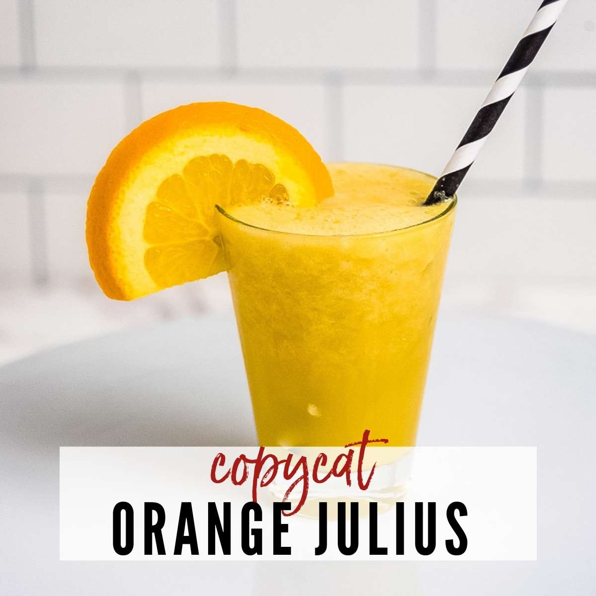 closeup of copycat Orange Julius with black & white straw & orange slice garnish on white background