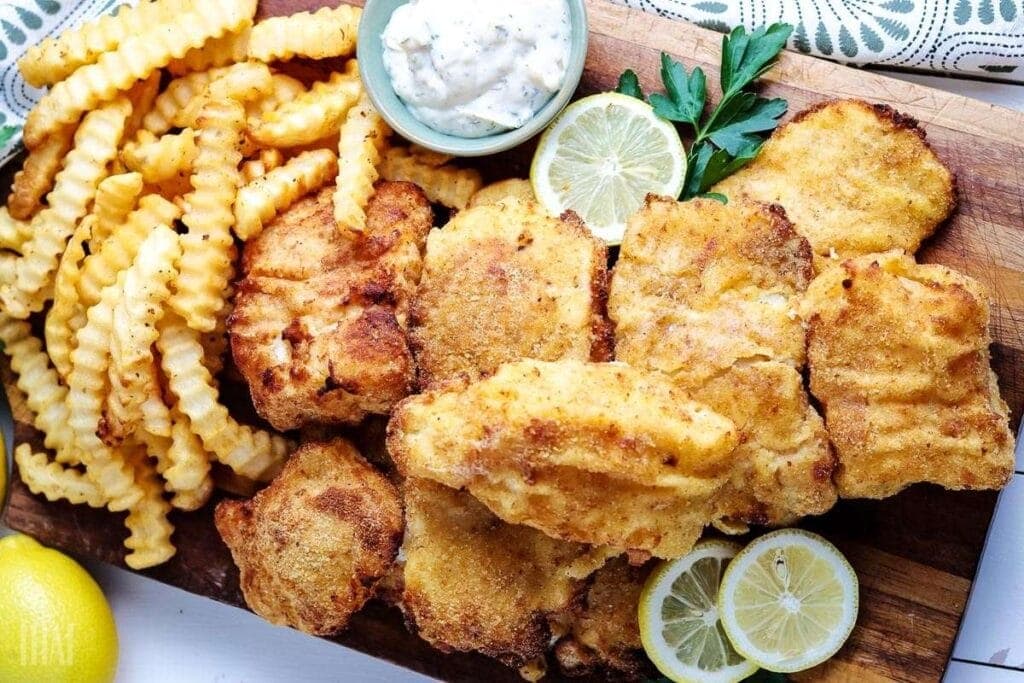 top view of crispy air fried cod next to french fries, lemon wedges, and tartar sauce