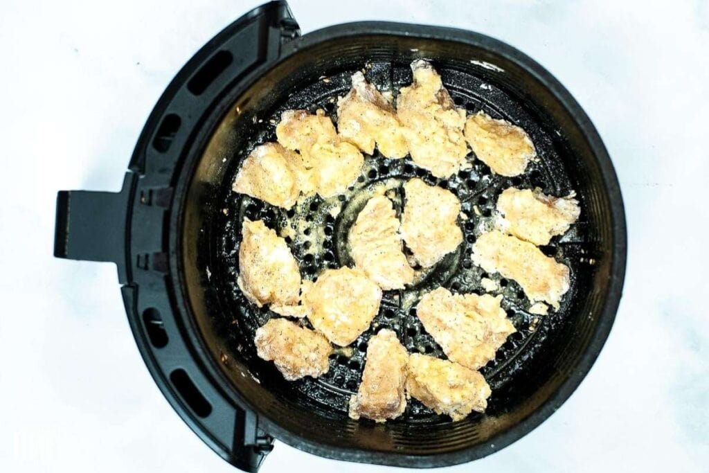 The uncooked, battered orange chicken pieces placed inside an air fryer basket.