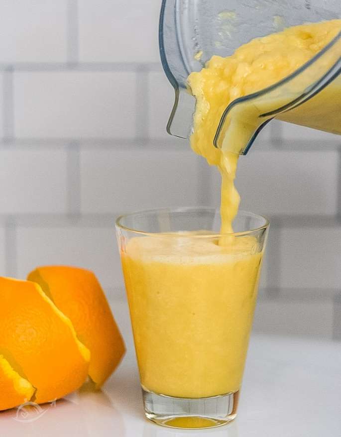 pouring blended drink into a clear glass on white background