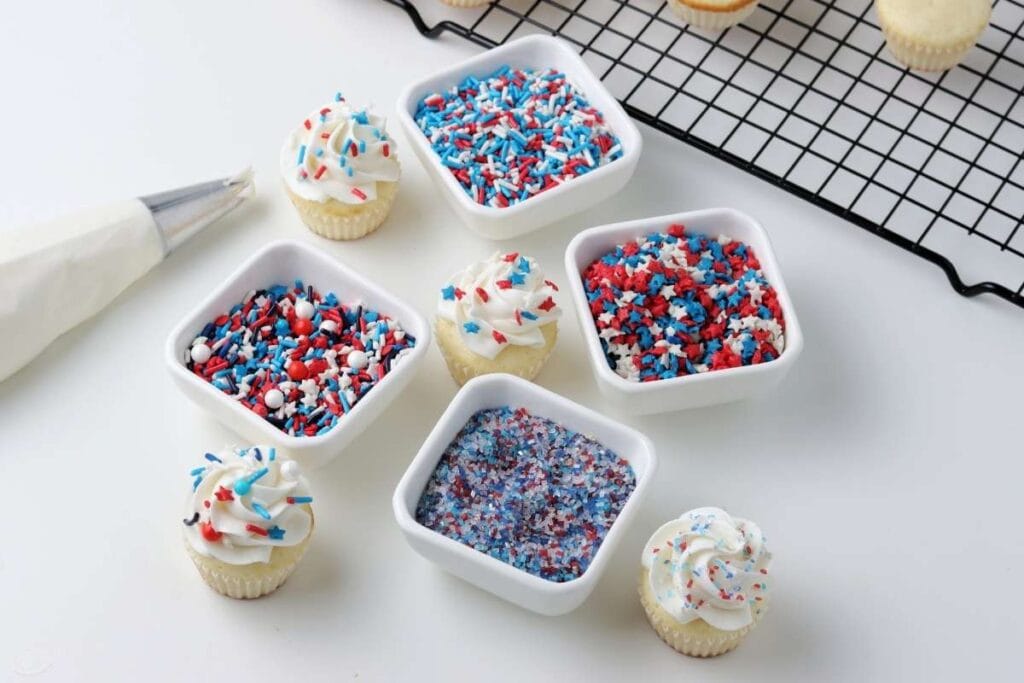 mini cupcakes decorate with red white and blue sprinkles next to icing bag