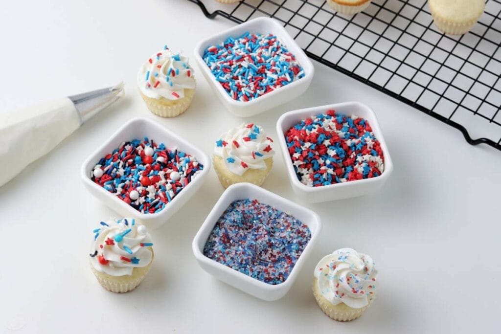 Mini cupcakes decorate with red white and blue sprinkles next to icing bag.