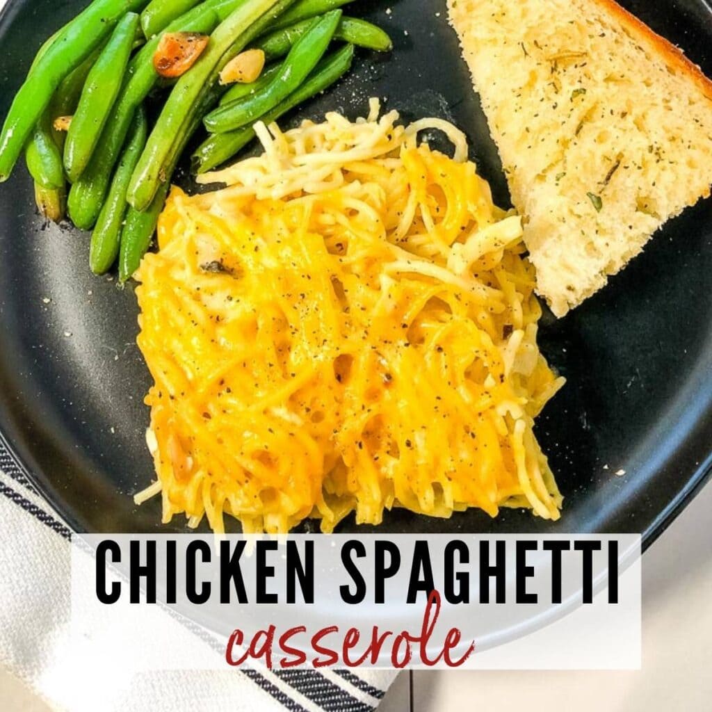 Slice of chicken spaghetti with green beans and garlic bread on a black plate with graphic overlay