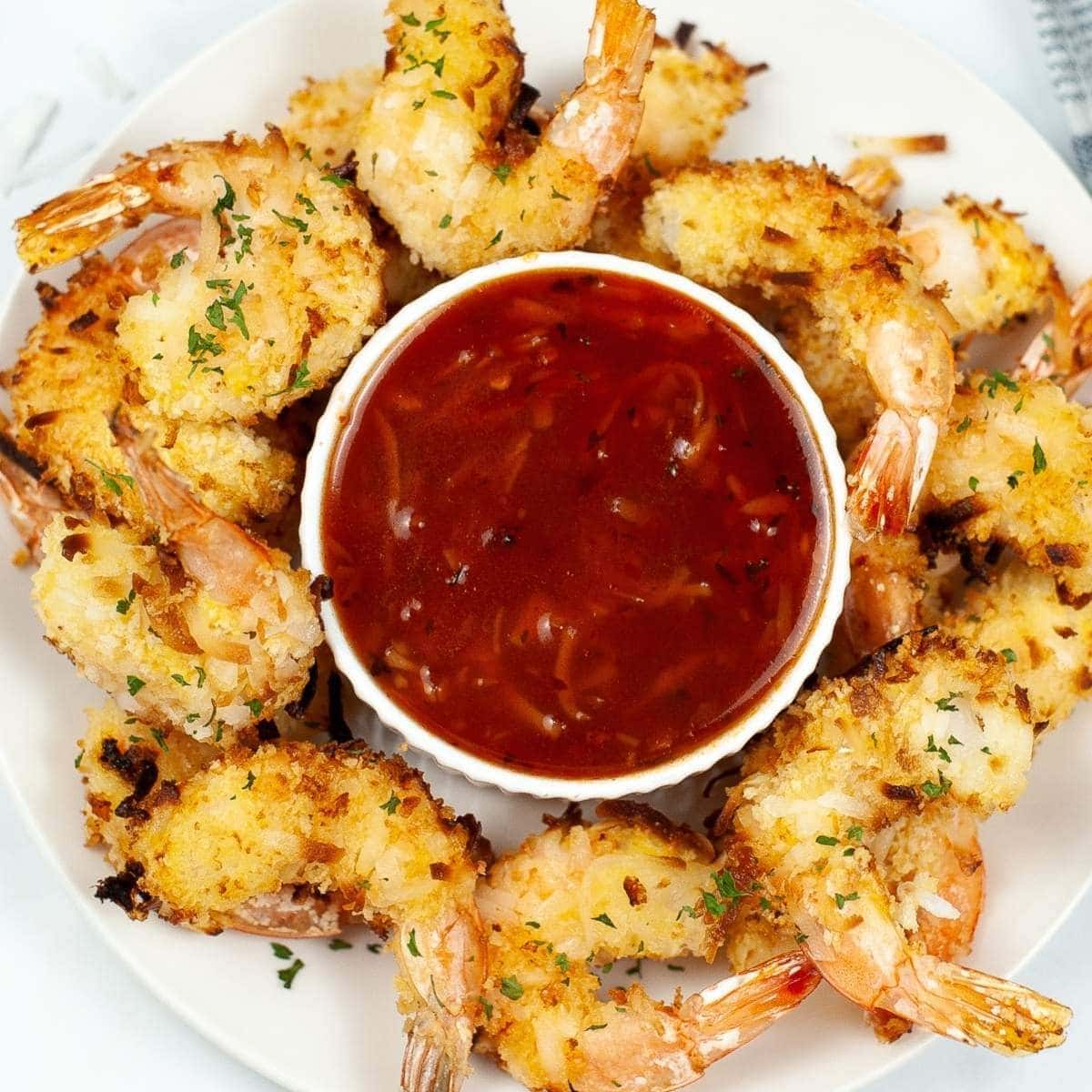air fried coconut shrimp arranged around a cup of sauce on a white plate