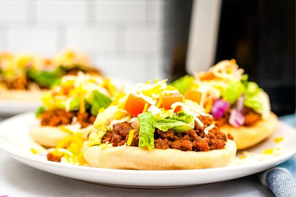 close up of air fryer navajo tacos after cooking with lettuce, cheese, tomatoes, and onions