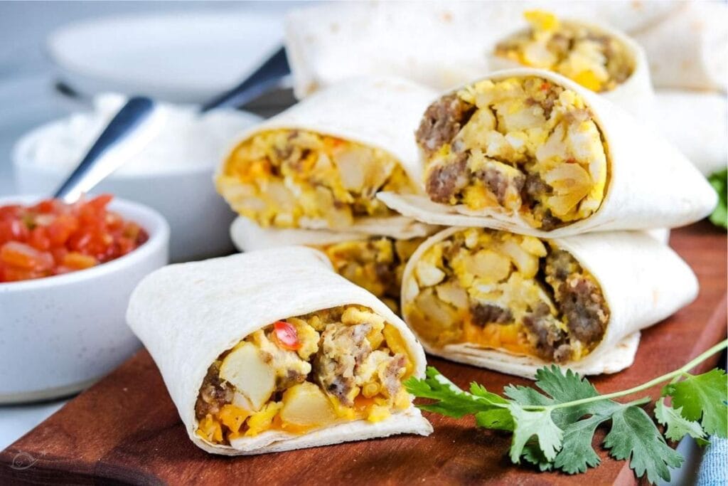 stack of breakfast burritos on a cutting board next to small bowl of salsa